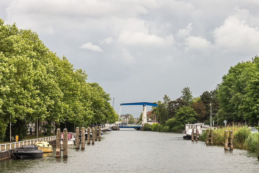 Kanaal in Diemen met aangemeerde bootjes, bomen langs de kade en de blauwe ophaalbrug in de verte