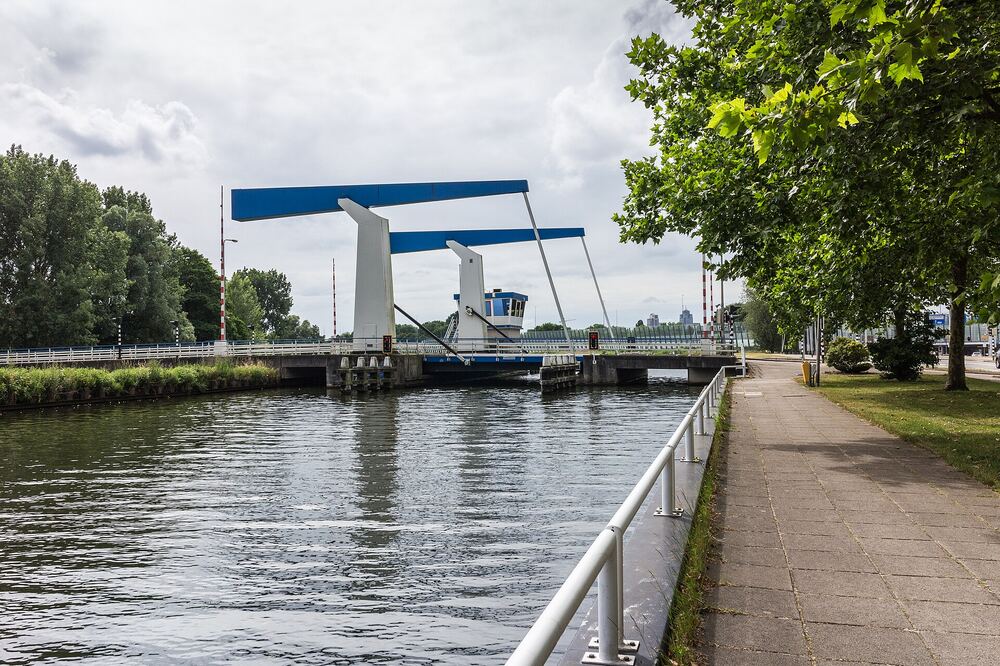 Blauwe ophaalbrug met geheven brugdek over het kanaal in Diemen, met een kade met plataan en brugwachtershuisje